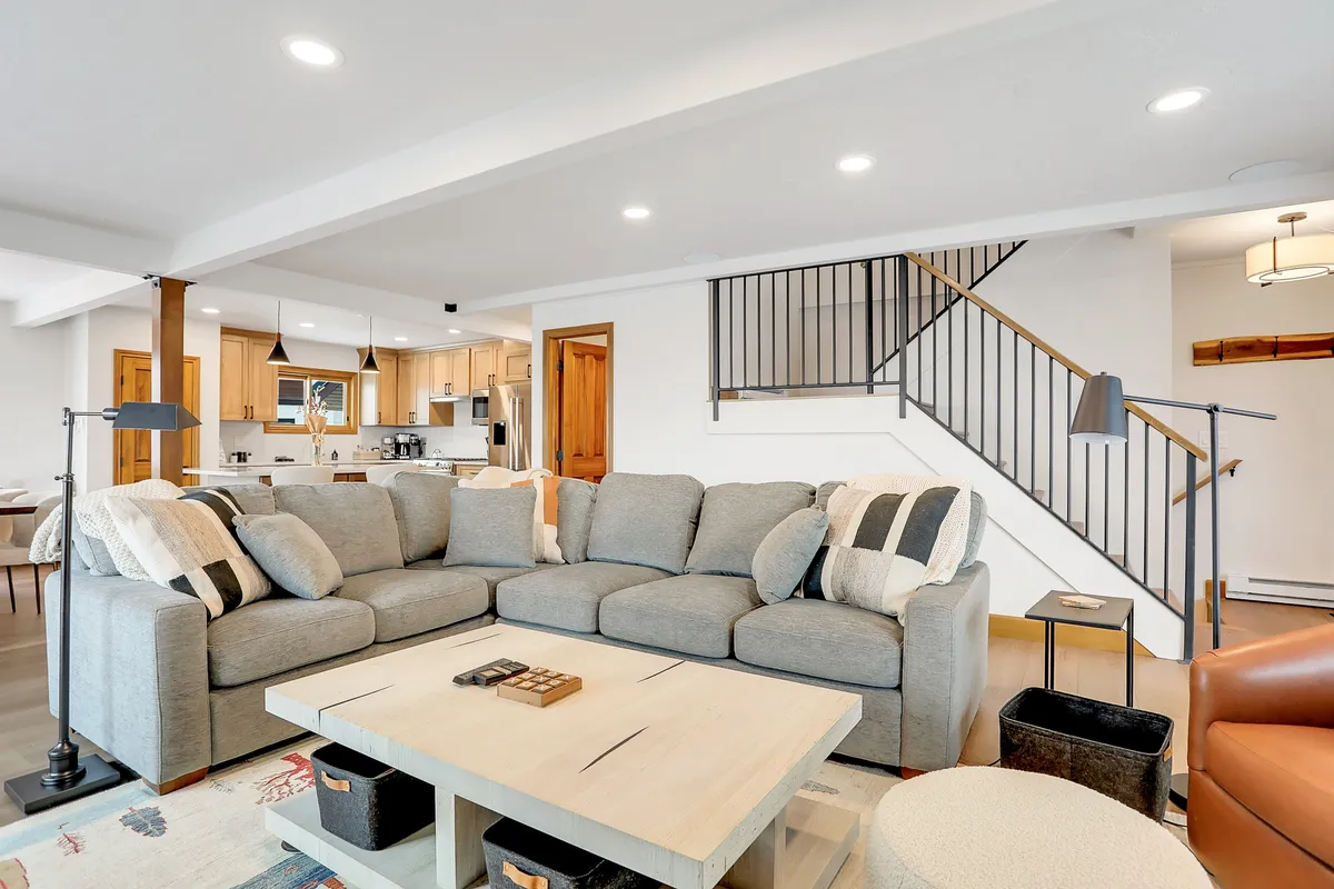 An inviting open-concept living space featuring a spacious sectional sofa, a coffee table central to the room, a staircase leading to the upper level, and a partial view into the adjacent kitchen area. The setup encourages gatherings, casual conversations, and shared activities such as game nights or movie watching.