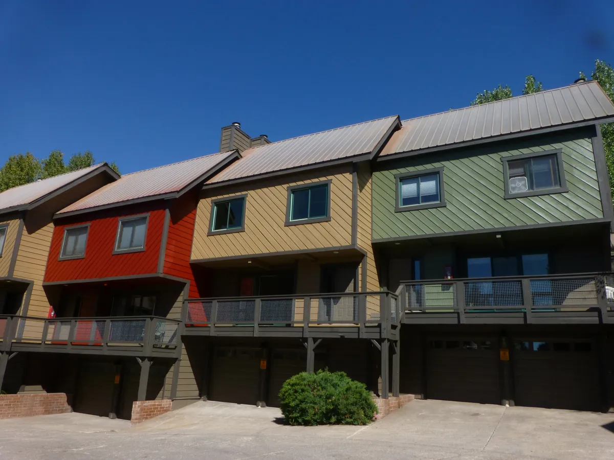 A vibrant exterior shot showing colorful condo facades with balconies and lush landscaping. The communal outdoor space suggests an energetic, friendly environment ideal for summertime gatherings, relaxation, and community events.