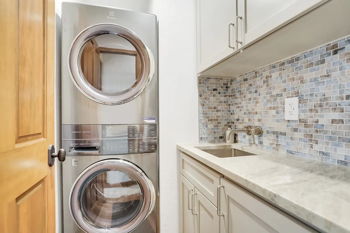A compact laundry area with stacked washer and dryer, complementary backsplash, and modern cabinetry. The efficient design is ideal for handling laundry tasks during a stay.