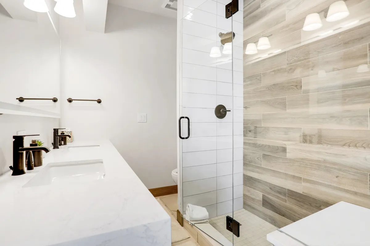 A modern bathroom with a double sink vanity, glass shower enclosure, and wood-like tile wall. The space feels fresh and tranquil, perfect for relaxing self-care routines.