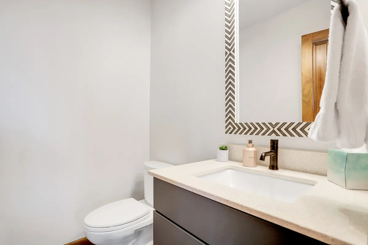 This image features a modern vanity with a mirror, sink, and toilet, capturing a clean and serene half-bath setup. The space is bright and organized, ideal for quick refreshes between outdoor activities or as a main-floor amenity.