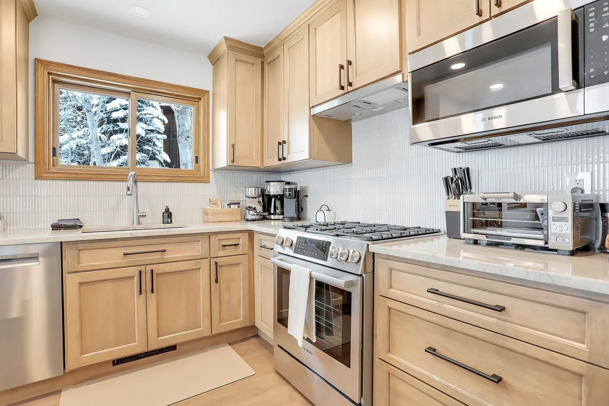 A bright, chef-inspired kitchen with stainless steel appliances, natural wood cabinetry, and a window revealing a snowy landscape. The space invites guests to cook together, share meals, and enjoy quality time in a functional, beautiful setting.