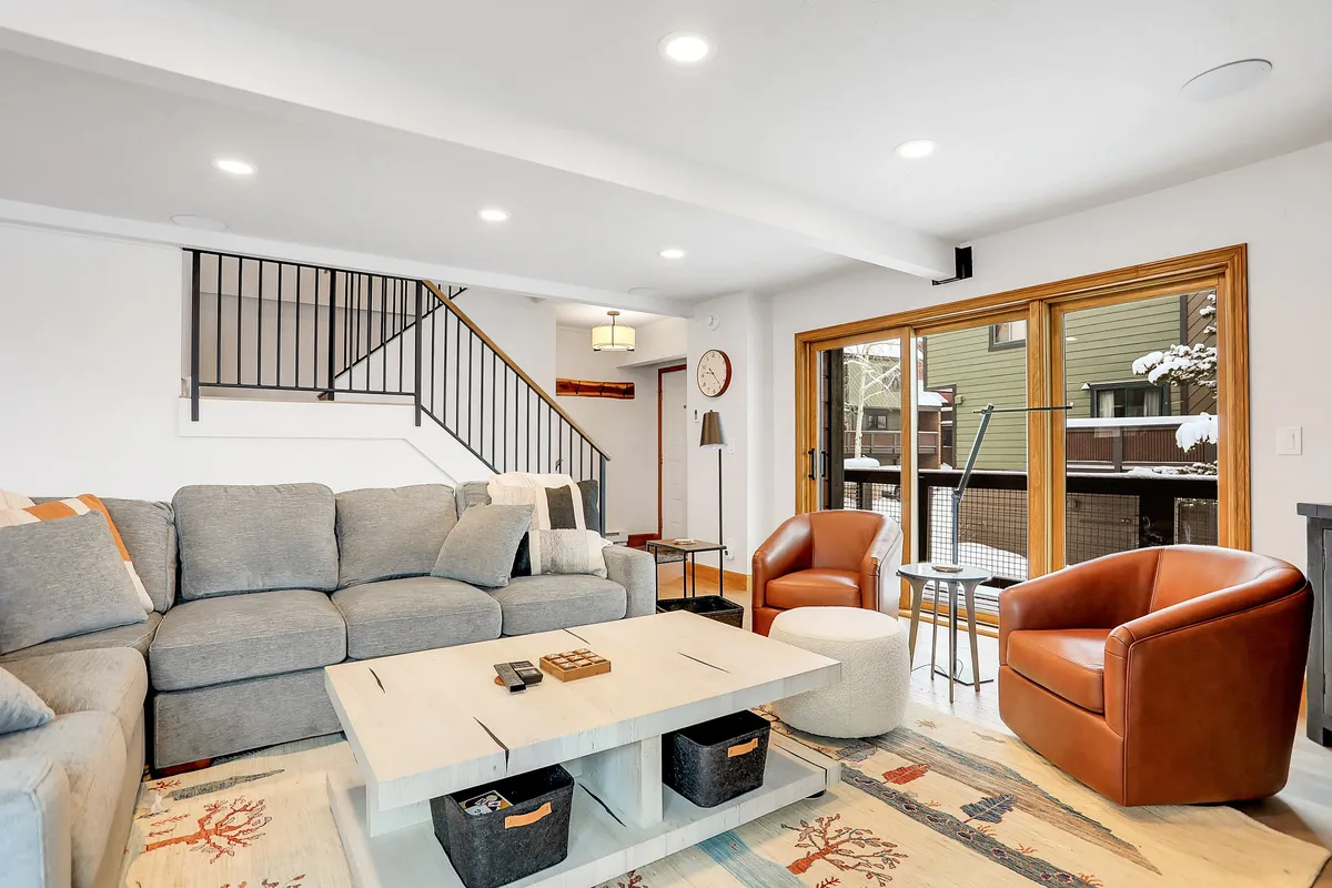 A stylish open-concept living space with a large sectional sofa, wooden coffee table, and two brown chairs, all oriented toward a sliding glass door that offers serene outdoor views. The room feels welcoming and perfect for socializing or unwinding after outdoor adventures.