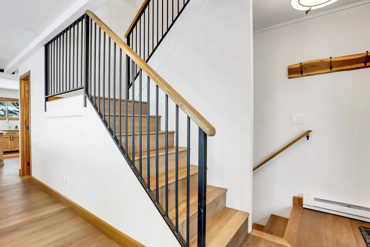 This image shows a staircase with a wooden railing and metal balusters, leading from one level to another within the home. The warm tones of the wood and the inviting feel suggest a welcoming transition space just inside the entryway—precisely where someone might enter from the garage or access the main floor amenities.