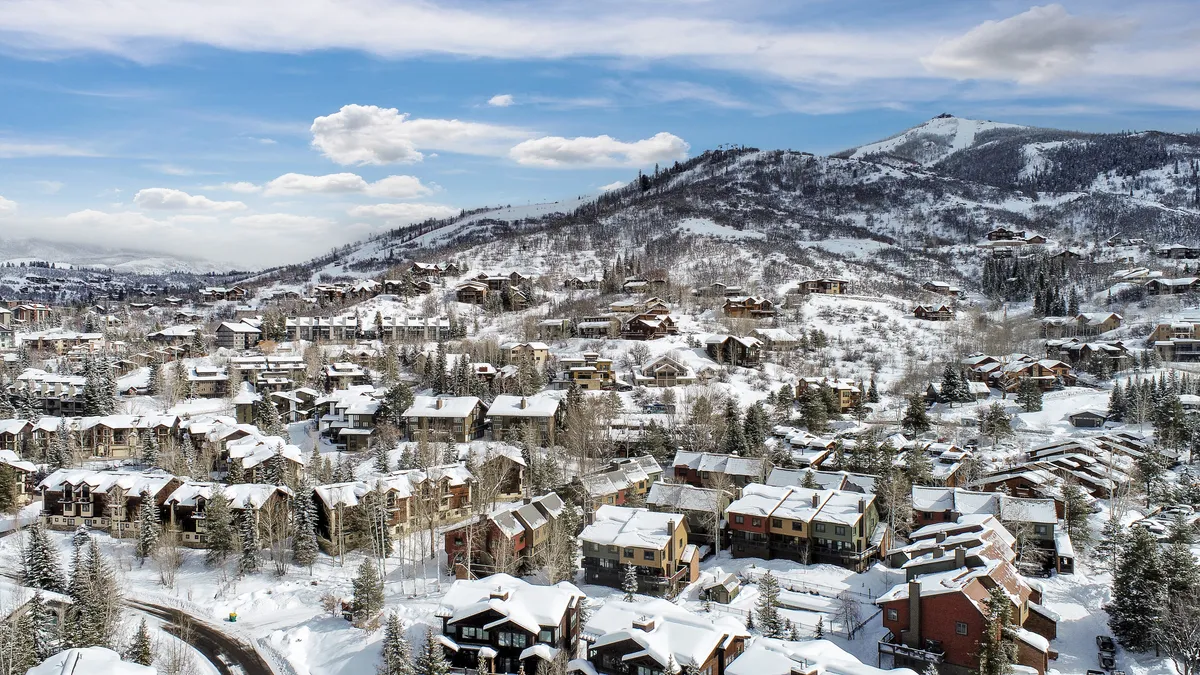 A snowy exterior shot featuring charming homes nestled beneath a distant mountain, framed by a tranquil tree line. The scene radiates the inviting atmosphere of an alpine community, with winter sports activities and local life just beyond the doorstep.