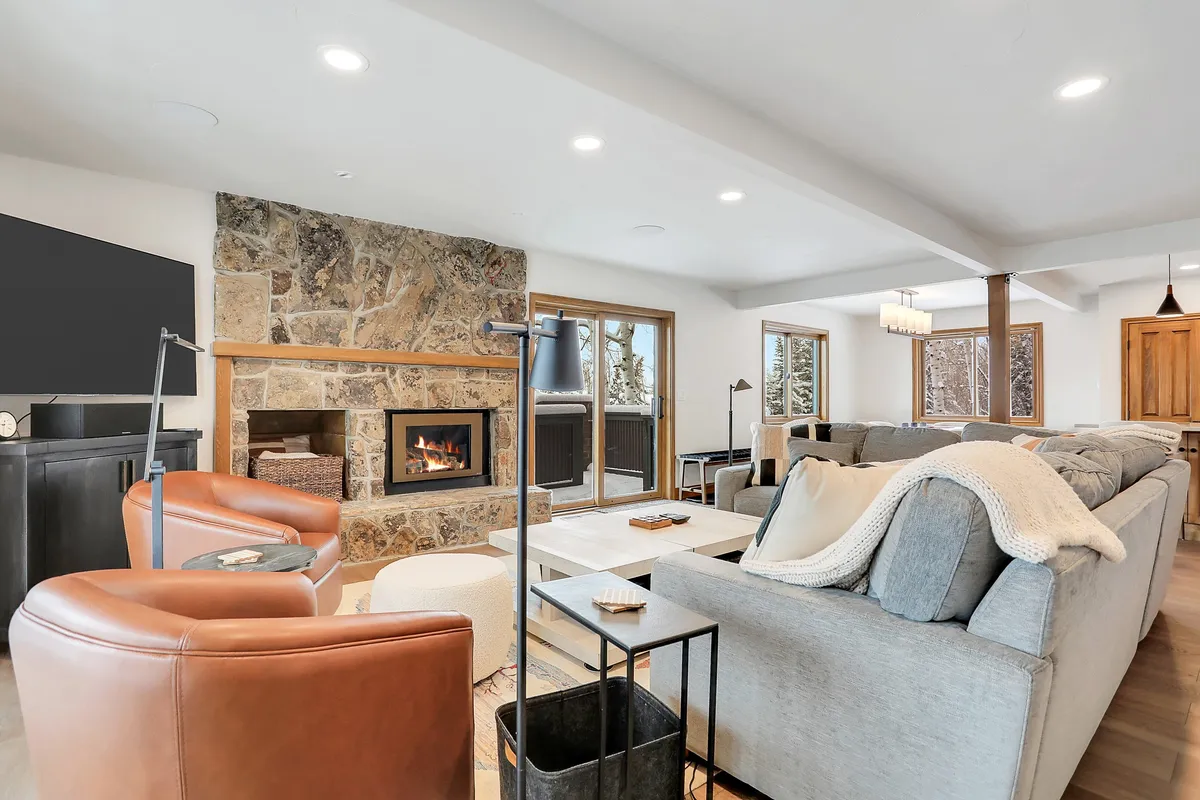 A cozy living area centered around a fireplace, with comfortable seating and large windows that invite in the natural light. Through the windows, you can glimpse the snowy landscape and feel a connection to the outdoors, while the inviting fire creates a warm, welcoming space to gather after a day of adventure.
