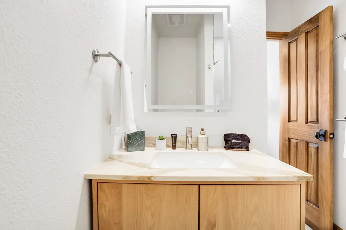 This image shows a vanity with sink and mirror next to a wooden door, offering a calm and inviting atmosphere. The adjacent door hints at the layout—potentially connecting to laundry or utility spaces commonly found near garage entries.