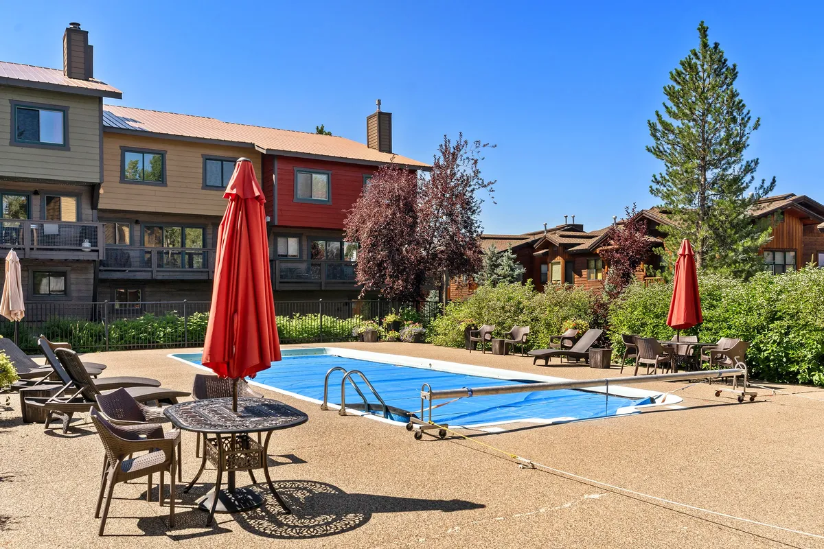 This image displays the community's sparkling outdoor swimming pool, surrounded by red umbrellas and an inviting seating area. The atmosphere is relaxed and perfect for social gatherings, sunbathing, or enjoying a refreshing swim during the warm months. The newly reconstructed pool area is showcased, with ample space for lounging and mingling.