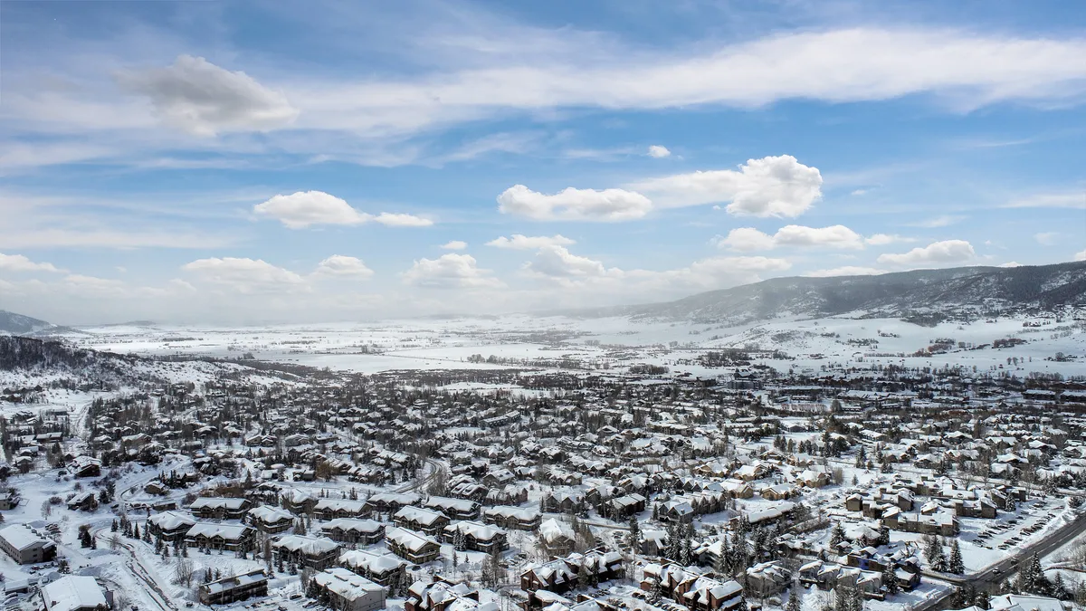 A wide view of snow-covered rooftops with distant mountains and an expansive sky, capturing the breathtaking scenery and open feel of Steamboat Springs in winter.